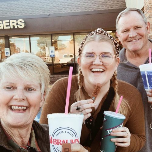A group of three people smiling and holding drinks outside a restaurant, enjoying a fun outing together.