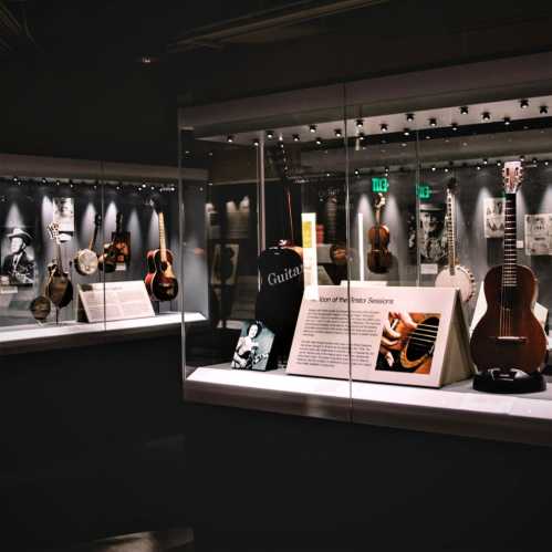 Display of various guitars and musical artifacts in a museum setting, with informational plaques and dim lighting.