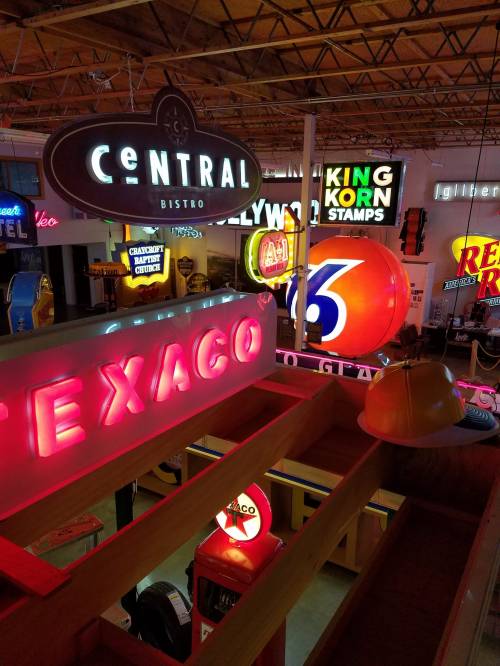 A vibrant display of vintage neon signs, including Texaco, Central Bistro, and King Korn Stamps, in a spacious venue.
