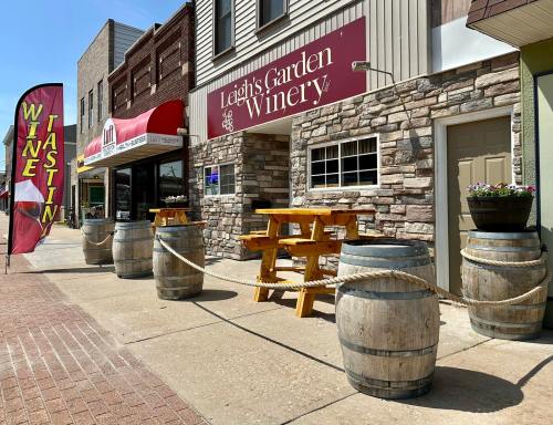 Exterior of Leigh's Garden Winery with wooden barrels, picnic tables, and a wine tasting sign on a sunny day.