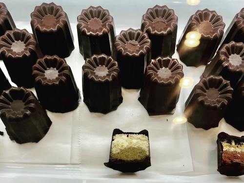 A display of chocolate-covered confections, some with a visible creamy filling, arranged neatly in a glass case.