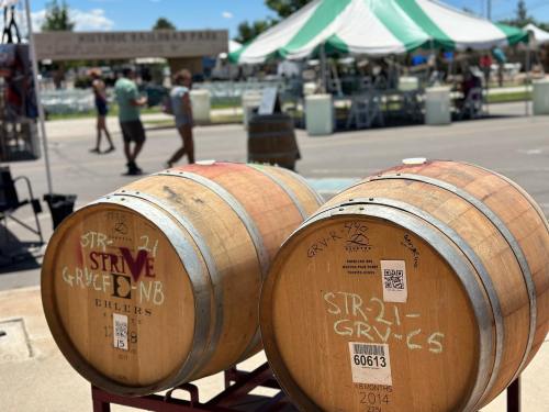 Two wooden wine barrels with labels, set in a festival atmosphere with tents in the background.