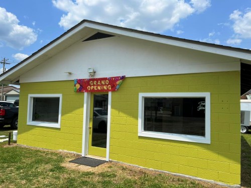 Bright yellow building with a "Grand Opening" banner, featuring large windows and a grassy area in front.