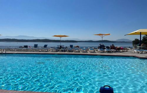 A clear blue pool with lounge chairs and yellow umbrellas, overlooking a serene lake and mountains in the background.