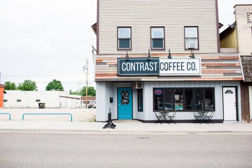 A coffee shop with a sign reading "Contrast Coffee Co." features a blue door and outdoor seating.