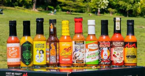 A variety of hot sauce bottles lined up outdoors, showcasing colorful labels and different flavors.