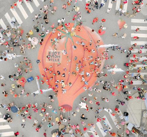 Aerial view of a large orange hot air balloon design on a street, surrounded by a crowd of people.
