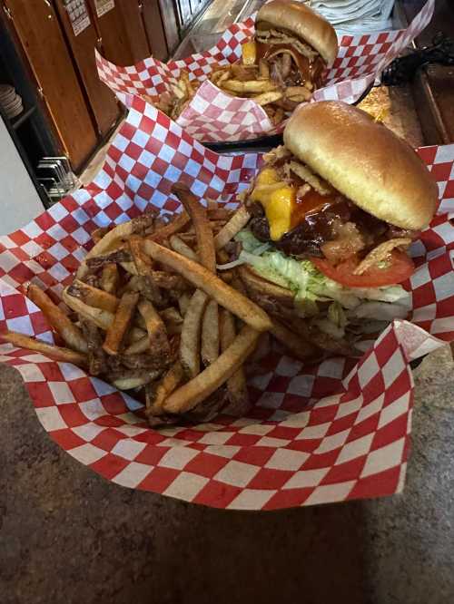 A delicious burger with toppings and a side of crispy fries, served in a red and white checkered basket.