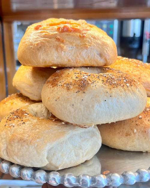 A stack of freshly baked bagels with various toppings, displayed on a silver platter.