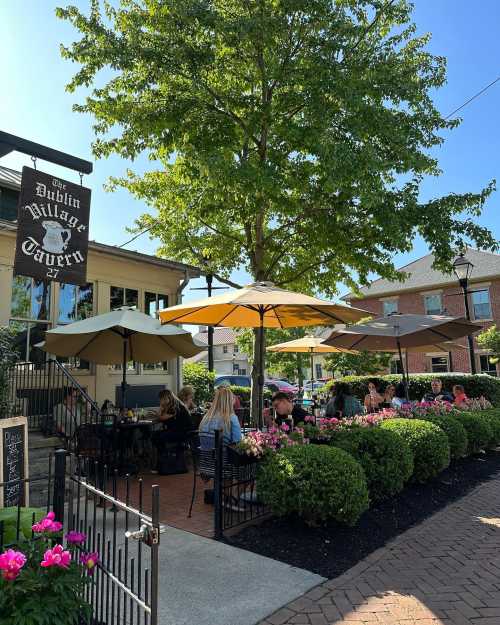 Outdoor dining area at Dublin Village Tavern, featuring umbrellas, greenery, and patrons enjoying their meals.