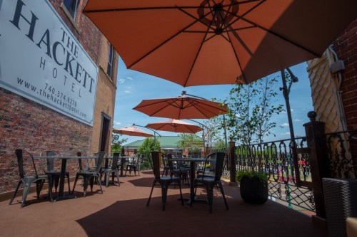 Outdoor seating area at The Hackett Hotel, featuring tables, chairs, and large umbrellas under a clear blue sky.