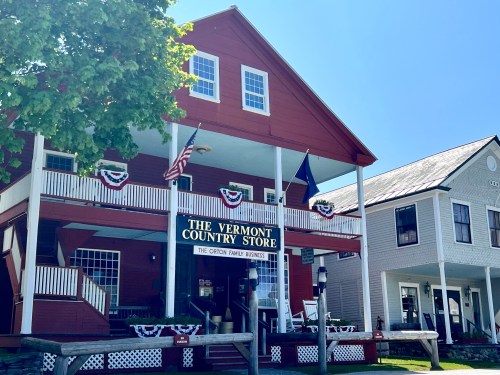 A red building with white trim, featuring a sign for "The Vermont Country Store" and decorated with flags and bunting.