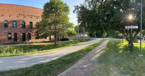 View of Adel City Hall with a tree, pathway, and sign marking the town of Adel in a sunny setting.