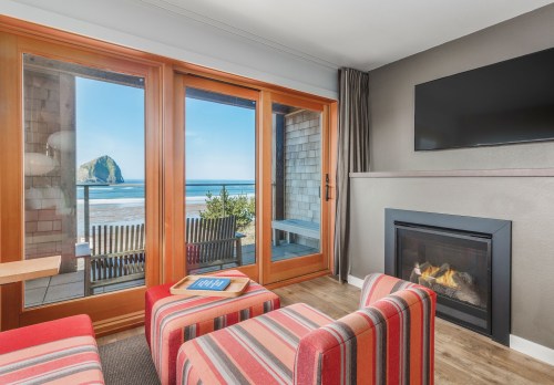 Cozy room with striped chairs, a fireplace, and large windows showcasing a beach view and a rock formation.