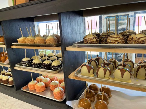 A display of various decorated caramel apples and cake pops on shelves, featuring chocolate and colorful toppings.