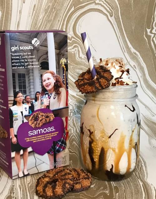 A jar of a milkshake topped with chocolate syrup and Girl Scout Samoas cookies, next to a box of Samoas.