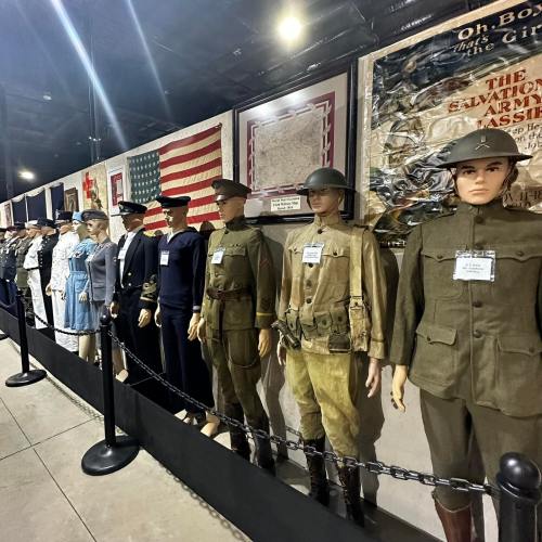 A display of mannequins in historical military uniforms, lined up against a backdrop of flags and posters.