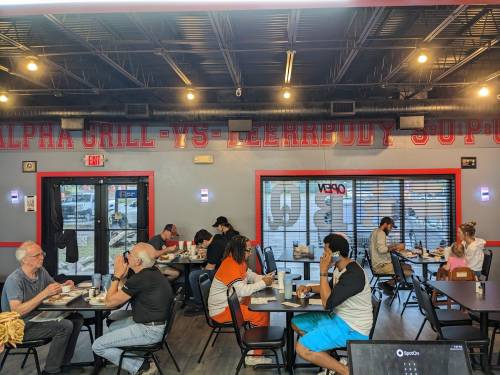 A busy restaurant interior with diners at tables, enjoying meals in a casual setting with a vibrant wall sign.