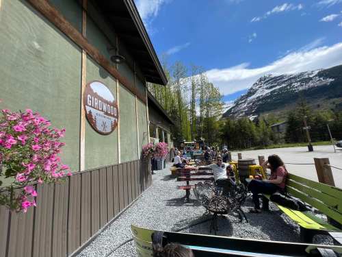 Outdoor seating area of a café in Girdwood, surrounded by flowers and mountains under a clear blue sky.