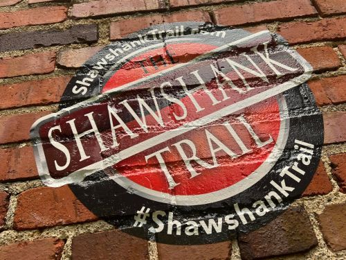 A circular logo on a brick wall promoting the Shawshank Trail, featuring the hashtag #ShawshankTrail.