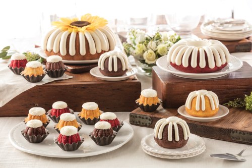 A variety of bundt cakes and mini bundt cakes with white frosting, displayed on wooden and white plates.