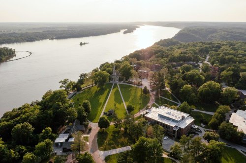 Aerial view of a river winding through lush greenery, with buildings and a park along the shore.