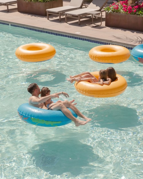 A man and two children float on colorful inner tubes in a pool, while two girls relax on another tube nearby.