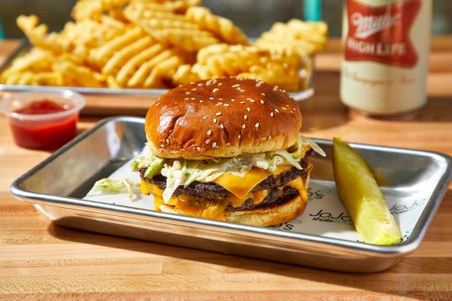 A juicy cheeseburger with lettuce on a sesame seed bun, served with crinkle fries and a pickle on a metal tray.