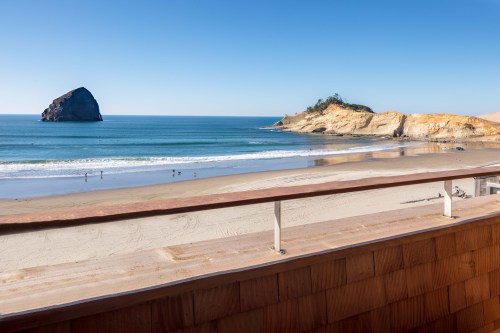 Scenic beach view with a rocky outcrop, clear blue sky, and gentle waves lapping at the shore.