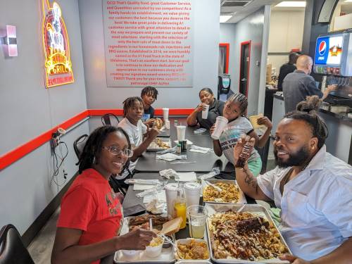 A group of six people enjoying a meal together at a restaurant, with large trays of food and drinks on the table.
