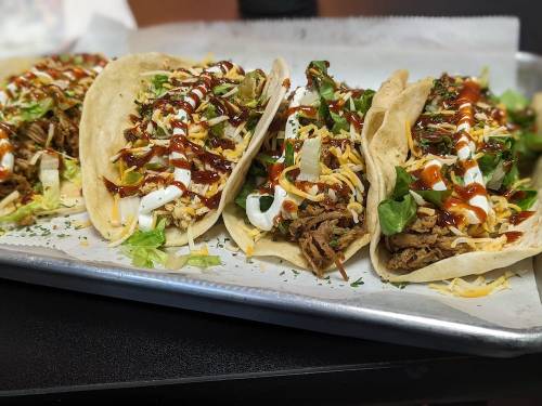 A tray of four tacos filled with shredded meat, lettuce, cheese, and drizzled with sauce and sour cream.
