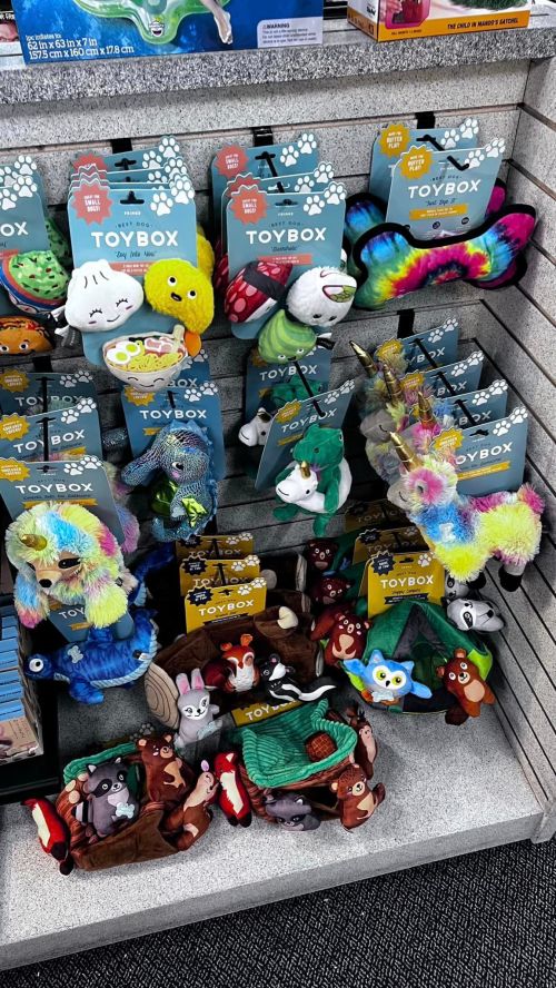 A display of colorful plush toys and pet accessories labeled "TOYBOX" on a store shelf.
