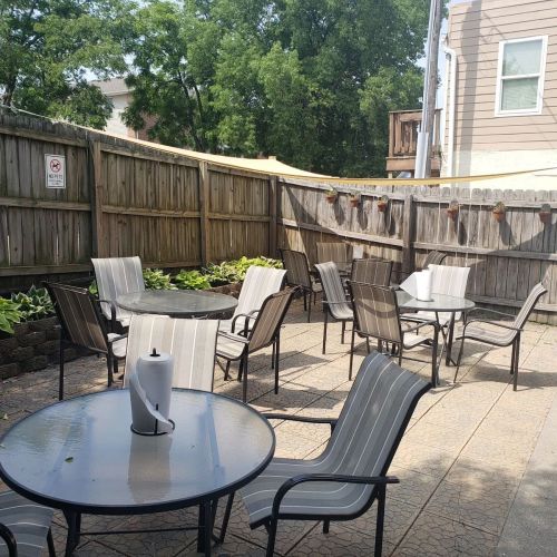 A small outdoor seating area with a round table and chairs, surrounded by greenery and wooden fencing.