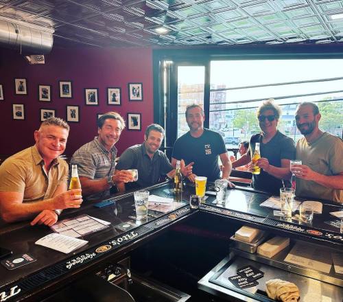 A group of six friends at a bar, smiling and holding drinks, enjoying their time together.