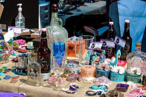 A vibrant display of various colorful bottles, glassware, and decorative items on a table at a market.