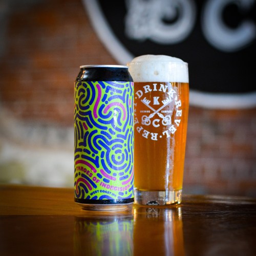 A colorful beer can next to a glass of golden beer with a foamy head, set against a rustic background.