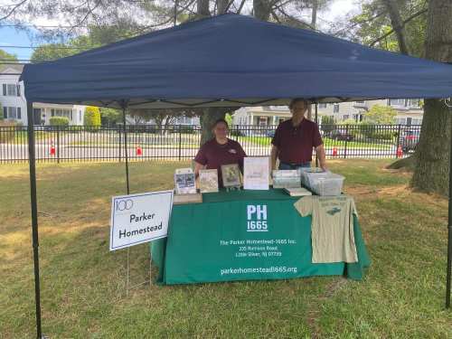 A booth at an outdoor event featuring two people, a green table with displays, and a sign for Parker Homestead.