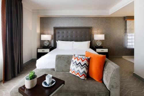 Cozy hotel room featuring a queen bed, decorative pillows, a small table with a cup, and stylish decor.