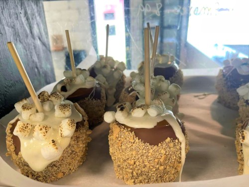 Delicious caramel apples coated in graham cracker crumbs, topped with chocolate and mini marshmallows on sticks.