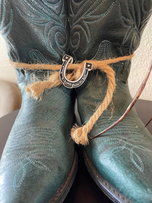 A pair of green cowboy boots tied with rope and a horseshoe charm, resting on a table.