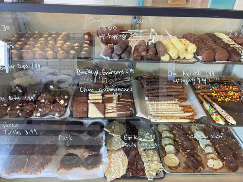 A display case filled with various chocolate treats, including marshmallows, pretzels, and graham crackers, with prices listed.