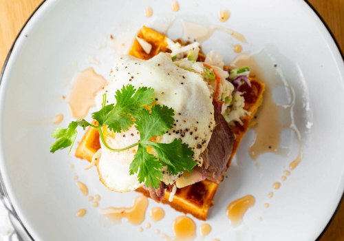 A plate featuring a waffle topped with pulled meat, a fried egg, and garnished with cilantro, drizzled with sauce.