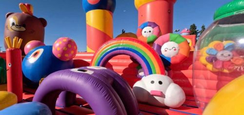 Colorful inflatable structures, including a rainbow and various cartoon-like characters, in a vibrant play area.