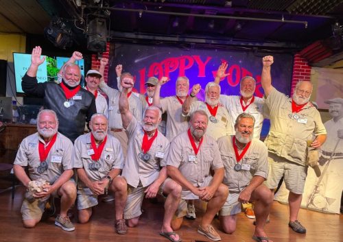 A group of men in matching outfits and red medals celebrate with raised fists in a lively venue.