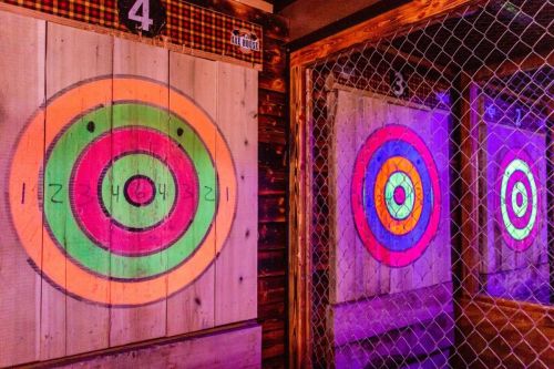 Two colorful dartboards with concentric circles, illuminated by purple lights, set in a rustic wooden environment.
