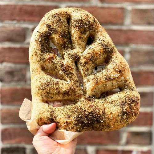 A hand holding a large, leaf-shaped piece of seasoned flatbread against a brick wall background.