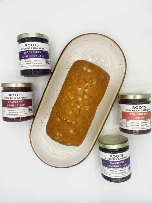 A loaf of bread on a plate surrounded by jars of various fruit jams.