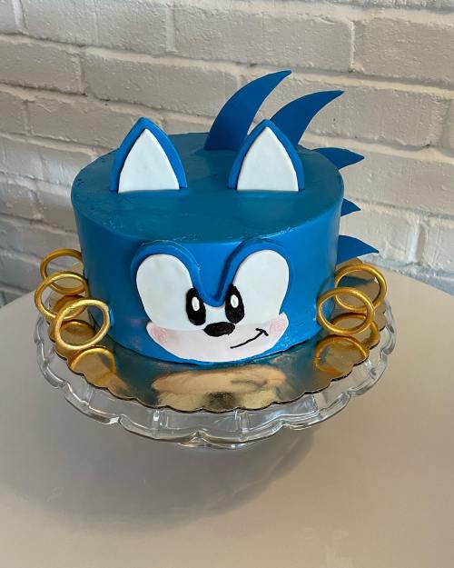 A blue cake decorated to resemble Sonic the Hedgehog, featuring his face and iconic rings on the sides.