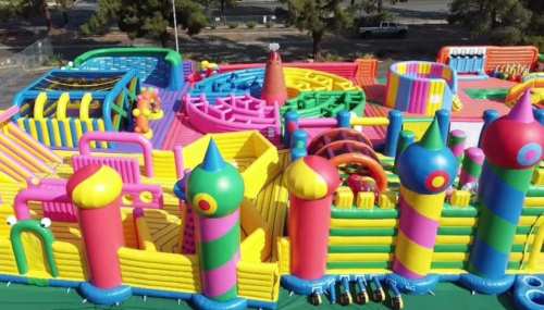 A colorful inflatable playground with slides, mazes, and various play structures in bright pink, yellow, and blue.