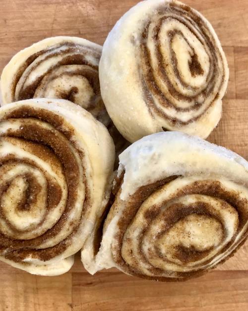 Four uncooked cinnamon rolls on a wooden surface, showcasing their swirled brown sugar and cinnamon filling.